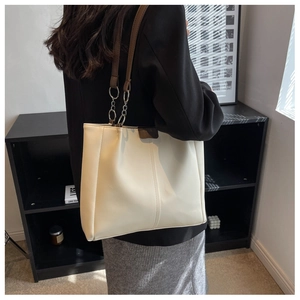 Detail of a large cream tote bag with brown straps and silver chain links for commuting