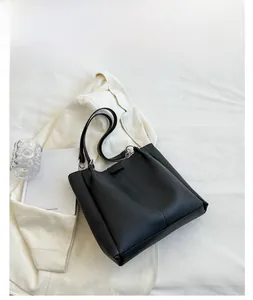 Detailed view of a black faux leather tote bag with slim shoulder straps on white fabric