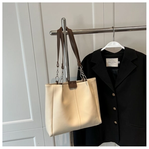 Detail of off-white tote bag featuring dark brown straps and silver chain hardware