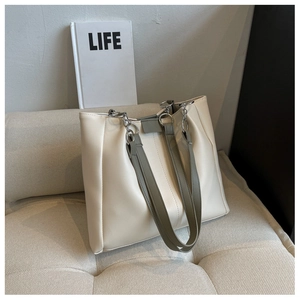 Minimalist cream white tote bag with grey straps resting on a soft fabric sofa