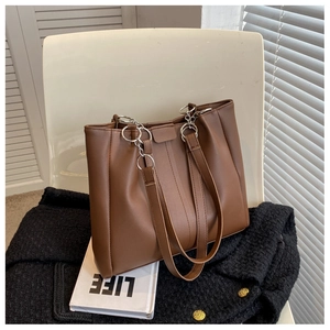 Detail of dark brown PU leather tote bag with silver chain straps on a white chair