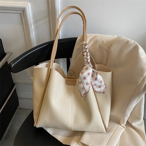 Large beige tote bag with brown trim and pink polka dot scarf on a black chair