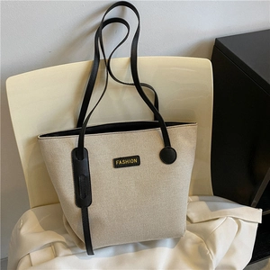 Minimalist beige large capacity canvas tote bag with black leather straps on a white chair