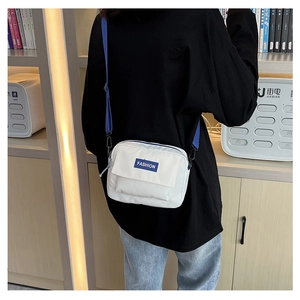 Detalle de bolso bandolera blanco con etiqueta azul y material de lona resistente
