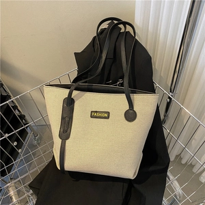 Minimalist beige canvas tote bag with black leather straps and fashion label in a basket