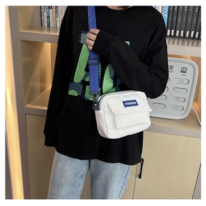 Detalle del bolso bandolera de lona blanca con etiqueta azul y correa ajustable