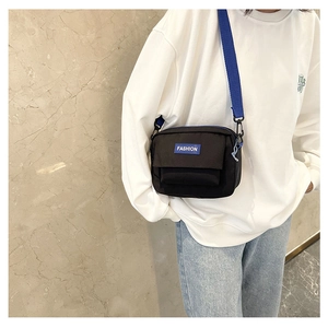 Detalle de bolso bandolera de nailon negro con correa azul y etiqueta en el modelo