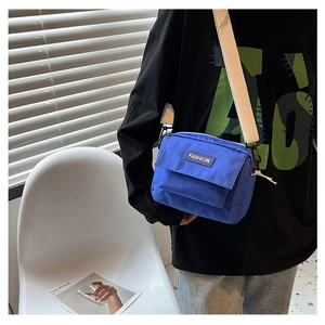 Detalle del bolso bandolera azul real con etiqueta FASHION negra y correa blanca