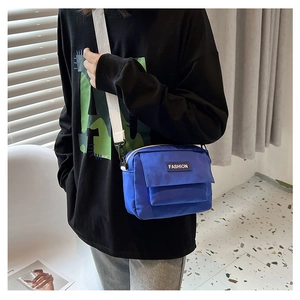 Primer plano de bolso bandolera azul con correa ajustable y parche logo en modelo hombre