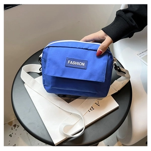 Detalle de un bolso bandolera azul minimalista de nailon con etiqueta Fashion y correa