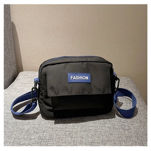 Detalle de bolso bandolera negro con etiqueta azul y textura de lona resistente