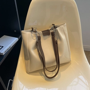 Large cream white tote bag with brown straps and silver chain detail on a chair