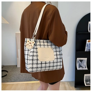 Detail of checkered tweed tote bag with beige leather pocket and cartoon cat charm