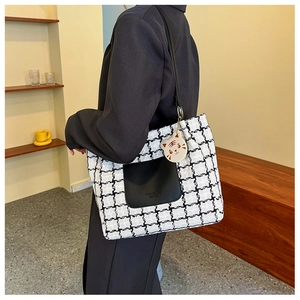 Detail of checkered tote bag with leather pocket and tiger charm on shoulder of model