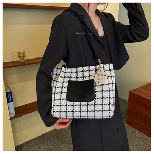 Macro view of checkered tweed tote bag featuring black leather front pocket and cat charm