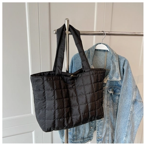 Detail of black quilted down tote bag hanging next to a denim jacket in indoor setting