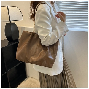 Vue détaillée d'un sac cabas marron brillant avec bandoulière chaîne dorée sur mannequin