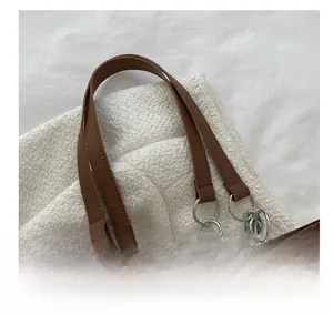 Detail of off-white textured tote bag with brown leather handle and silver metal rings