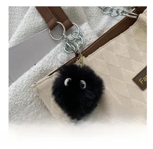 Close-up of a black fluffy keychain with eyes on a beige quilted shoulder bag