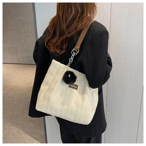 Detailed back view of a beige quilted tote bag with brown straps and plush ball charm