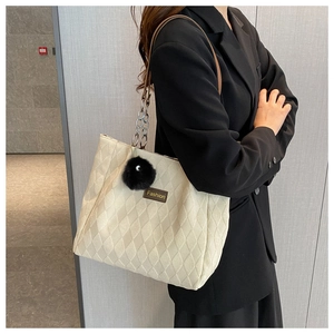 Detail of cream quilted tote bag featuring leather chain strap and black fur pom pom charm