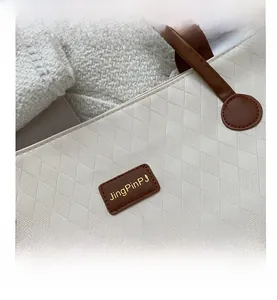 Close-up of quilted cream faux leather tote bag with brown straps and golden logo