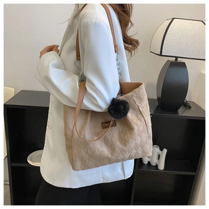 Detail of beige quilted tote bag with brown chain strap and black plush ball pendant