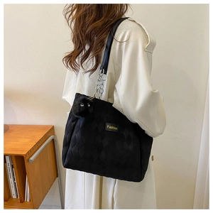 Detail of black quilted tote bag with wide strap and plush monster charm on model