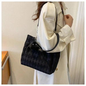 Close-up of black quilted tote bag with cute plush monster charm and fashion label tag