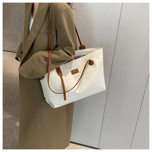 Close-up of woven cream tote bag with brown leather straps worn with a brown coat