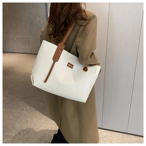 Detail of white tote bag featuring fine texture, brown leather straps and a minimalist logo