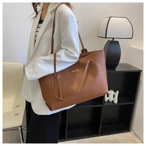 Detail of a brown quilted leather tote bag with a golden logo plate and shoulder strap