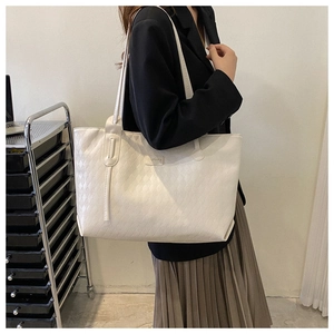 Detail of white large tote bag with diamond quilted pattern and metal logo plate