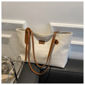 Detail of beige quilted tote bag with brown straps and logo on a leather sofa