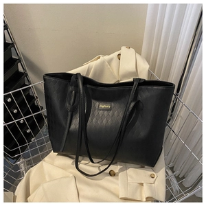 Detail of black tote bag featuring woven texture finish and gold metal logo plaque