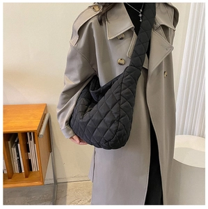 Detail of black quilted hobo bag with diamond pattern on a grey trench coat model