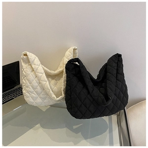 Close-up of quilted large cloud tote bags in cream and black on a glass desk surface