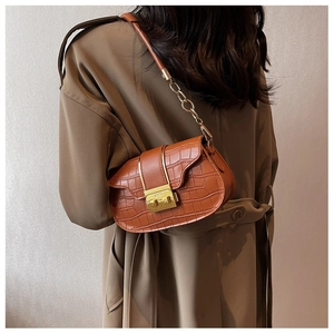 Detail of a brown crocodile pattern saddle bag with gold chain strap on a trench coat