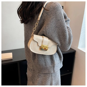 Detail of cream crossbody bag with crocodile texture and gold chain strap on model
