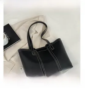 Detail view of large black tote bag with white contrast stitching on a beige blazer