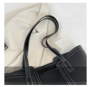 Detail view of durable black leather tote shoulder strap with contrast white stitching
