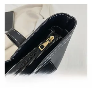 Close-up of smooth gold metal zipper and white contrast stitching on black leather tote bag