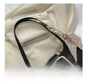 Close-up of black crocodile-textured leather handbag with gold buckle and silk scarf