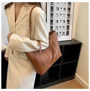 Detail of caramel leather tote bag showing white contrast stitching and minimalist design