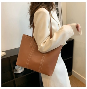 Detail of caramel brown leather tote bag with white stitching shown on a model