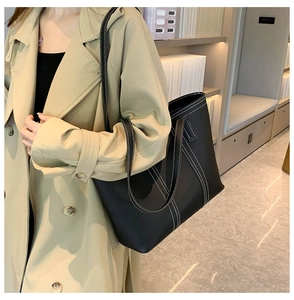 Detail of a large black tote bag with white contrast stitching on a model in trench coat