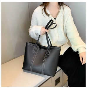 Detail of a black leather tote bag featuring contrast white stitching and long shoulder straps