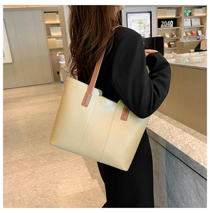 Detail of a beige tote bag with vertical stitching and brown handles in a cozy library setting