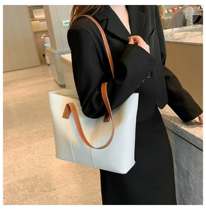 Detail of a large cream tote bag with brown contrast straps and vertical stitching