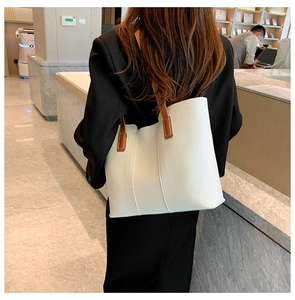 Detail view of large white tote bag with brown leather handles worn over the shoulder